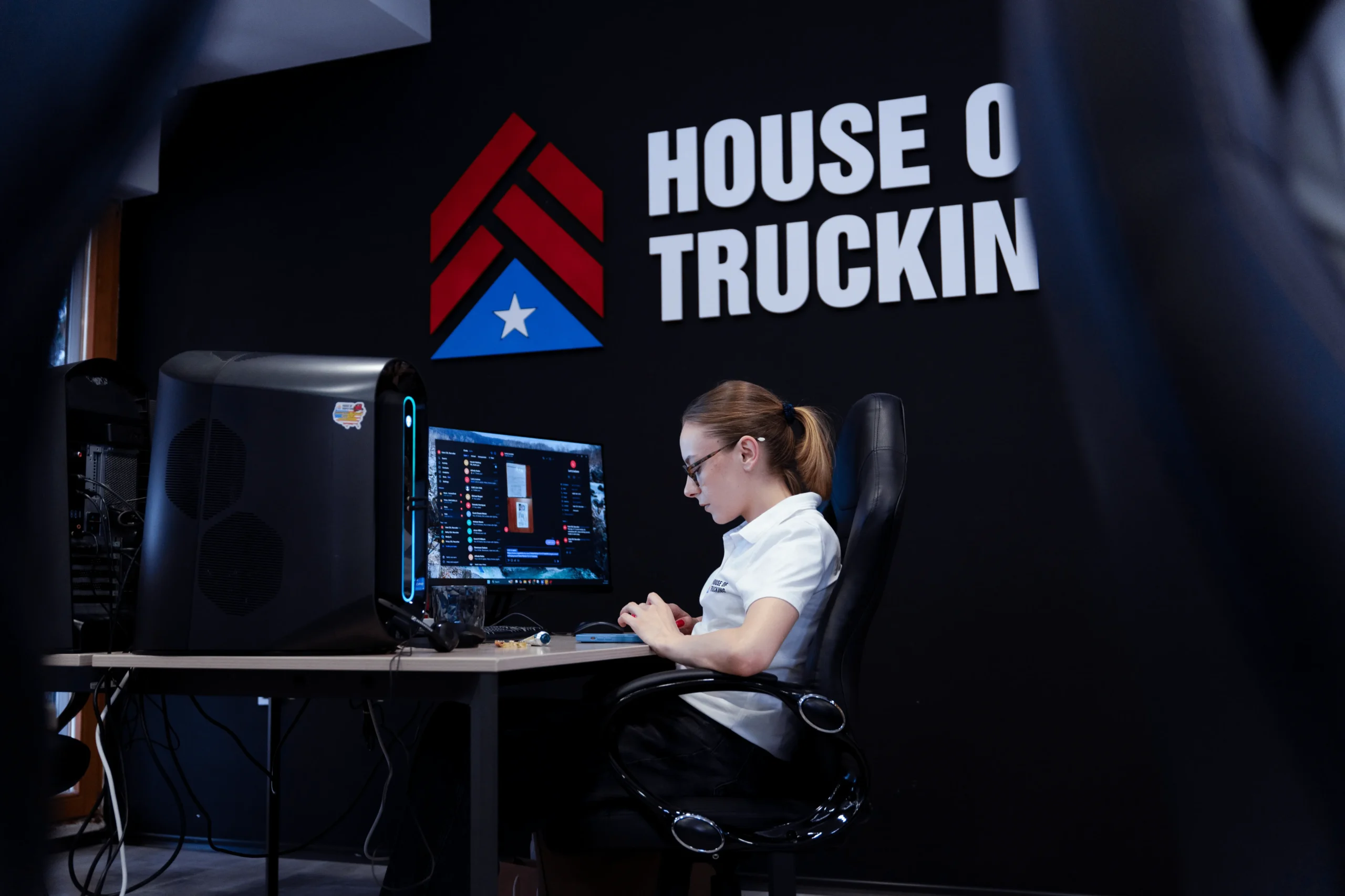 House of Trucking employee working at a computer station with company logo on the wall