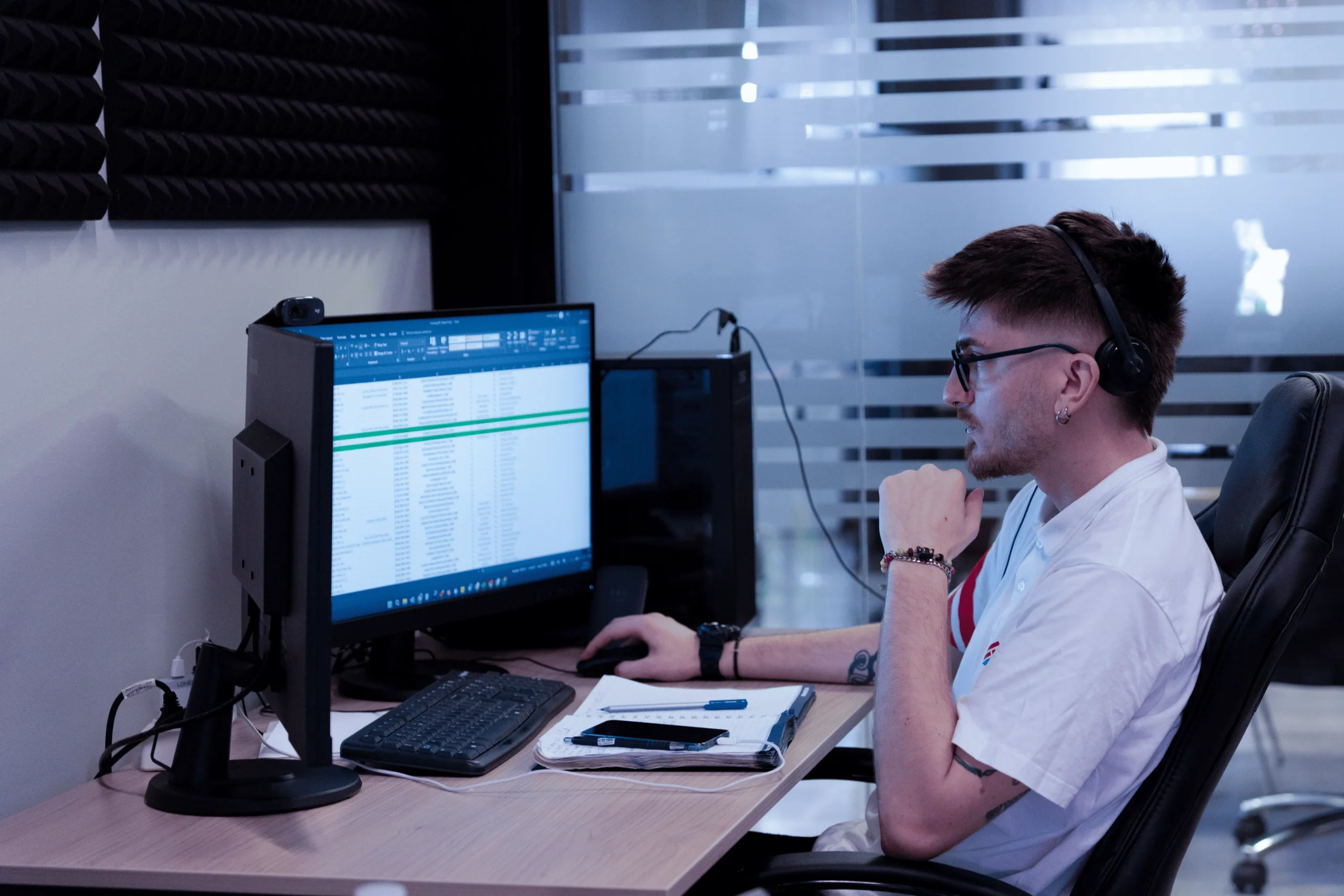 Dispatcher working at computer with headset, managing fleet data and maintenance schedules.