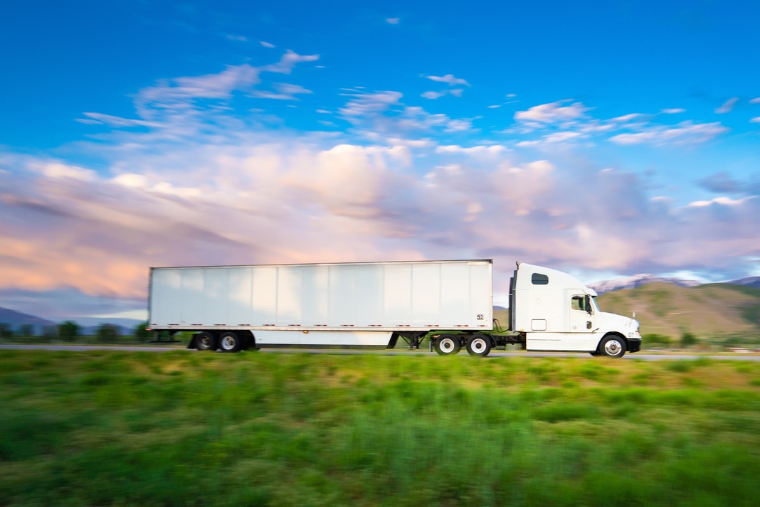 White dry van semi-truck driving on highway with mountains in background