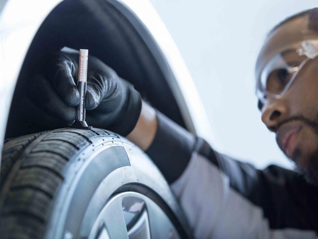 Mechanic measuring tire tread depth to meet DOT safety regulations